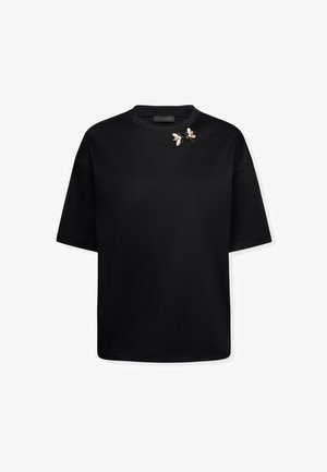 Czarna koszulka z krótkim rękawem i okrągłym dekoltem, ozdobiona dwiema złotymi i białymi przypinkami w kształcie pszczół w pobliżu dekoltu.