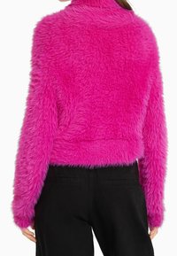 Faux-Fur-Cropped-Jacke in lebhaftem Pink mit flauschiger Textur und langen Ärmeln, kombiniert mit schwarzen Hosen. Keine sichtbaren Beschläge oder Akzente.
