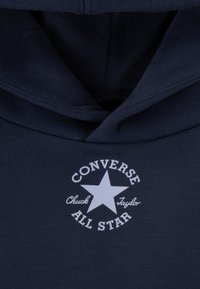 Navy hoodie made of soft fabric features a white printed logo with a star, text "CONVERSE", and "Chuck Taylor" beneath it.
