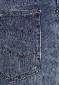 Jeans in denim blu scuro con una tasca posteriore caratterizzata da cuciture gialle e una leggera texture. Il tessuto presenta un classico motivo intrecciato.