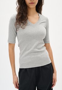 Ljusgrå, ribbad, kortärmad V-ringad topp av mjukt material. Figursydd design med slät textur, kombinerad med svarta, löst sittande byxor.