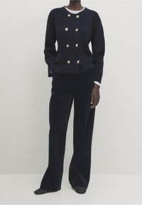 Granatowy sweter dzianinowy z guzikami w złotym odcieniu, z okrągłym dekoltem i długimi rękawami, w połączeniu z pasującymi szerokimi spodniami z weluru.