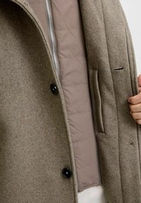 Pruun villase coat, millel on silebeez vooder, varustatud lukuga, kahe musta nupuga ja külgpocketiga siseosas.