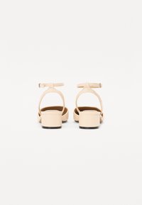 Sandales à talons beiges avec un dos fermé, une bride autour de la cheville et un talon block. Fini en cuir lisse avec des éléments de design minimalistes.