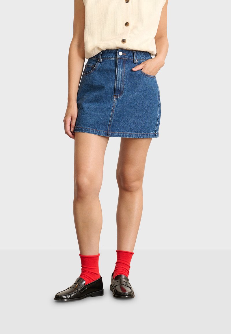 Jeanskjol i blått med en åtsittande midja, fem fickor och knappstängning. Matchas med svarta loafers och röda knästrumpor.