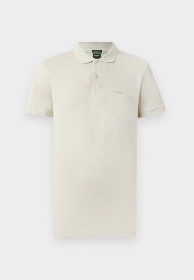 Polo en coton beige clair, doté d'un col classique, de manches courtes, d'une patte à deux boutons et d'un logo brodé discret sur la poitrine.