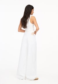 Weiße weite Hosen mit hoher Taille und großen Gesäßtaschen. Begleitet von einem enganliegenden weißen Tanktop, das einen lässigen Look präsentiert.