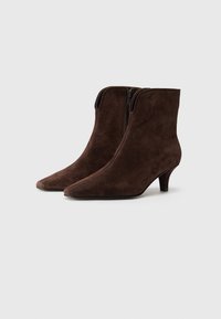 Bottes de cheville en suede marron avec un bout pointu et un petit talon. Elles disposent d'une fermeture éclair à l'arrière et d'une finition lisse et texturée.