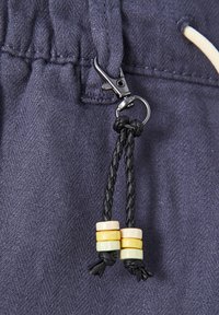 Tissu bleu marine avec un tissage texturé, doté d'un clip en métal et d'un cordon noir tressé agrémenté de trois perles en bois colorées.