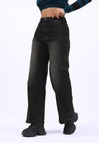 Jeans de pierna ancha negra con un acabado desgastado, cintura alta y bolsillos delanteros. Combinados con zapatillas negras texturizadas.