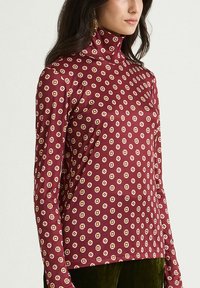 Maglietta dolcevita a maniche lunghe color bordeaux con motivo geometrico ripetuto in crema e rosa. Tessuto liscio con design aderente.