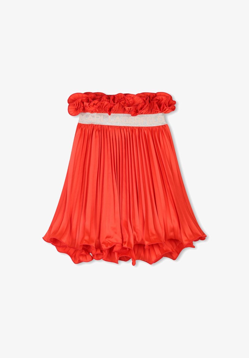 Jupe plissée rouge avec un bandeau supérieur élastique froncé, ornée d'une bande logo contrastante. Fabriquée en tissu léger et lisse. L'ourlet est légèrement arrondi.