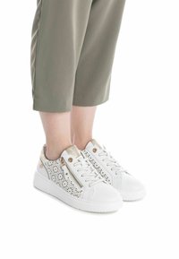 Zapatillas blancas con un diseño perforado en el costado, acentos dorados y tela texturizada en el talón. Suelas planas y cierre con cordones.