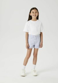 Un short en denim bleu clair avec des bords effilochés, associé à un t-shirt en coton blanc. Des baskets blanches et des chaussettes montantes complètent le look.