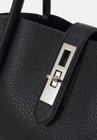 Czarna skórzana torebka o teksturowanym wykończeniu, z prostokątnym srebrnym zapięciem i podwójnymi uchwytami do noszenia.