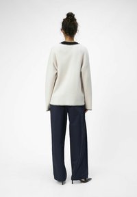 Lys grå oversized sweater med sort kant, parret med marineblå vide bukser. Glat tekstur, afslappet pasform og enkelt design.