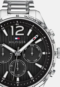 Montre en acier inoxydable argenté avec un cadran texturé noir, dotée de trois sous-cadrans, d'index horaires blancs et d'une échelle tachymétrique sur la lunette.