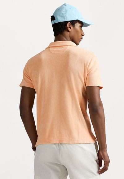 Korte mouw, lichtoranje polo met een gestructureerde stof, voorzien van een standaardkraag en een relaxed fit, gecombineerd met een lichtblauwe pet.