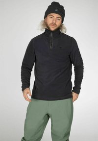 Pullover in pile nero con zip a quarto di giro, caratterizzato da un logo sottile sul petto. Abbinato a pantaloni verde chiaro a vestibilità rilassata. Tessuto caldo e testurizzato.