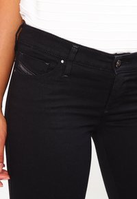 Svarta denimjeans med figurnära design, utrustade med en liten framficka och knäppning med en toppknapp. Minimalistisk sömnad och detaljer i metal.