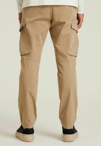 Khaakiowe spodnie cargo o luźnym kroju, z dużymi bocznymi kieszeniami, gładką bawełnianą teksturą oraz elastycznymi mankietami u kostek.