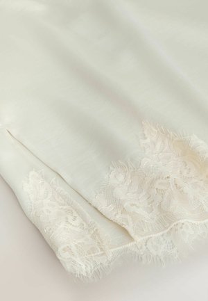 Měkká bílá látka s jemnou květinovou krajkou podél okrajů, zobrazující jemnou texturu a složité detaily.
