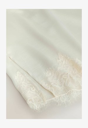 Měkká bílá látka s jemnou květinovou krajkou podél okrajů, zobrazující jemnou texturu a složité detaily.