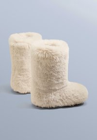 Krém színű, bolyhos csizma puha, bársonyos külsővel, lekerekített formával és széles nyílással a tetején, ideális a melegség és kényelem érdekében.