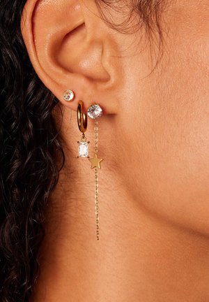 Gouden oorbellen met meerdere ontwerpen: een kleine kristallen studs, een hangende rechthoekige edelsteen en een sterrenhangertje aan een ketting.