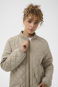 Quiltet beige jakke med høj krave, guld lynlås og elastiske manchetter. Har diamantformet syning og sidelommer.