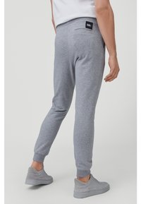 Grey cotton sweatpants with tapered legs, elastic waistband, side pockets, and a small black label on the back pocket.
