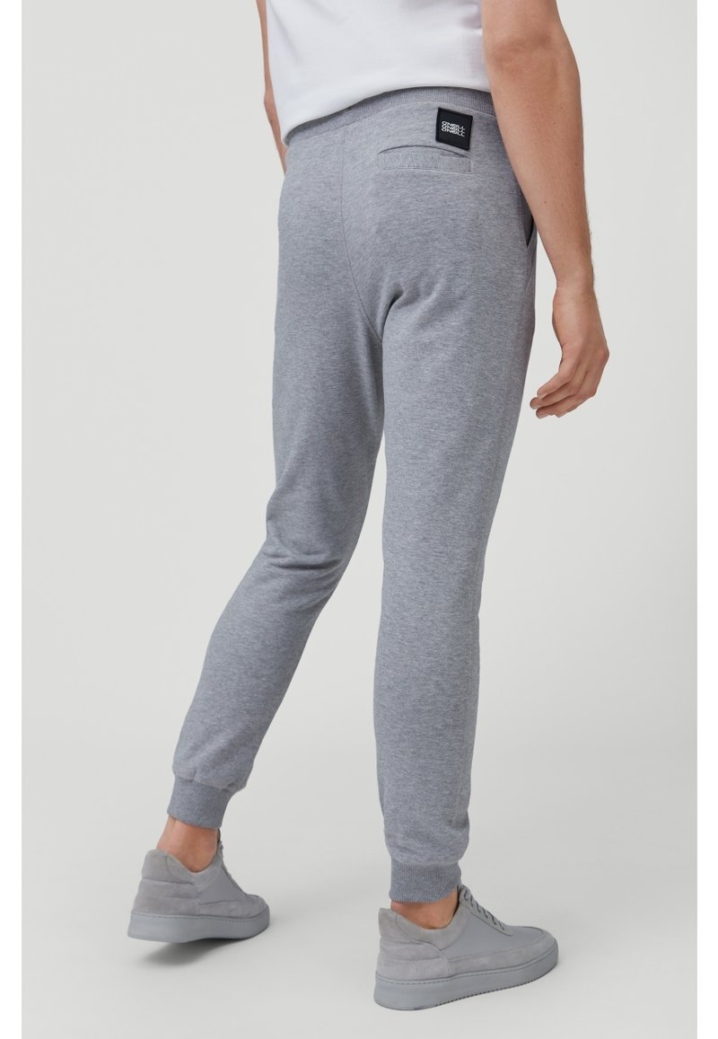 Pantaloni tuta grigi in cotone con gambe affusolate, cintura elastica, tasche laterali e una piccola etichetta nera sulla tasca posteriore.