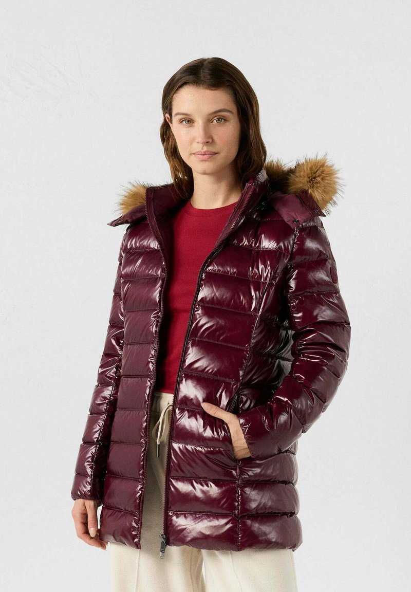 Giacca imbottita color bordeaux con finitura lucida, design trapuntato orizzontale e cappuccio staccabile in pelliccia sintetica. Dotata di tasche con cerniera.