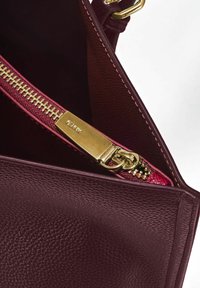 Wnętrze bordowej skórzanej torebki z złotym zamkiem błyskawicznym, charakteryzujące się teksturowaną powierzchnią i kontrastową różową podszewką z tkaniny.