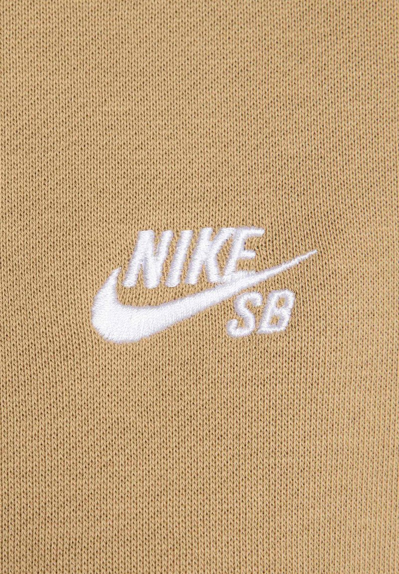 Beżowa dzianina z białym haftowanym logo "NIKE SB", o gładkiej fakturze i czystym wzornictwie.