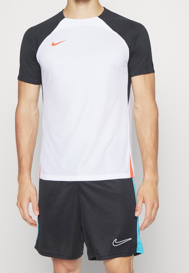 Camisa deportiva de Nike con mangas raglán cortas negras, cuerpo blanco y logotipo naranja brillante. Pantalones cortos negros con acentos azules y logotipo blanco.