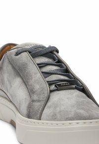 Sneaker grigio in suede con una texture liscia, caratterizzato da lacci blu, una suola in gomma piatta e un dettaglio metallico vicino ai lacci.