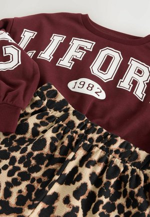 Un sweat-shirt bordeaux avec un texte blanc "GLIFOR" et un emblème "1982" au-dessus d'une jupe texturée imprimée léopard. Ceinture élastique sur la jupe.