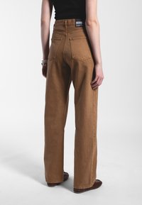 Jeans a vita alta, marroni, con gamba larga e finitura texturizzata, dotati di due tasche posteriori e un'etichetta del marchio sulla cintura.