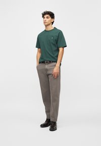 Ciemnozielona bawełniana koszulka z krótkim rękawem, z małym logo. Szare spodnie o prostych nogawkach, lekko luźne. Czarne sznurowane buty o gładkiej fakturze.