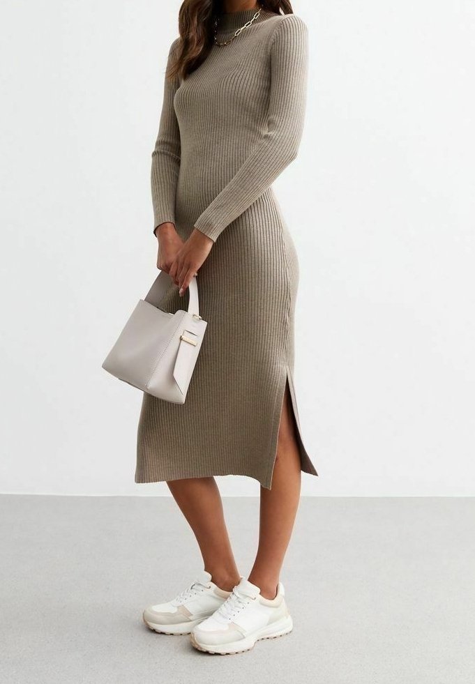 Femme en robe midi beige côtelée avec fente latérale, baskets blanches, collier chaîne en or, tenant un sac à main gris clair.