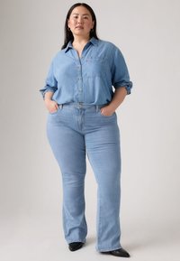 Svijetloplava traper košulja s gumbima i džepom na prsima, uparena sa svijetloplavim zvonastim trapericama. Crna obuća upotpunjuje odjevnu kombinaciju.