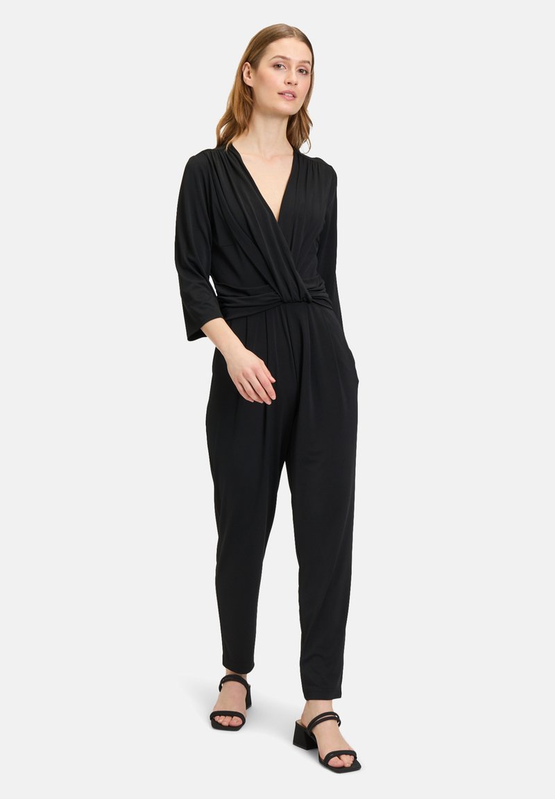 Tuta nera con scollatura a V profonda, design drappeggiato, maniche a tre quarti e vestibilità morbida. Abbinata a sandali neri con tacco a blocco.