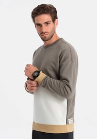 Grå og hvid farveblokeret sweatshirt med ribbede manchetter og kant. Udstyret med et logo-patch nederst og et struktureret stof.