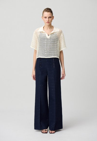 Haut en tricot de style crochet crème avec un col, assorti à un pantalon large bleu marine avec des accents de boutons et des rayures verticales subtiles.