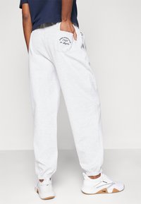 Grijze joggingbroek met elastische boorden en een achterzak met geborduurde tekst. Gecombineerd met witte sportschoenen.