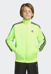 Neon zelena jakna sa zipom, visokim ovratnikom, zip džepovima i crnim trostrukim dizajnom na rukavima. Adidas logo na prsima.