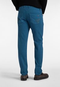 Turkizne hlače z gladko teksturo, ki imajo zadnje žepke s kontrastnim šivom in ožji kroj.