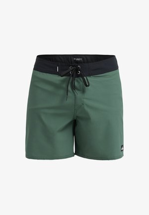 Shorts de bain verts avec une ceinture élastique noire. Dotés d'une fermeture à cordon et d'une petite étiquette logo sur l'ourlet inférieur. Texture lisse.