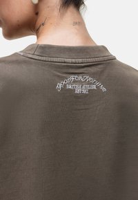 Olijfgroene katoenen t-shirt met een ronde hals en geborduurd logo op de achterkant met de tekst "GOOD FOR NOTHING BRITISH ATELIER EST 2011."